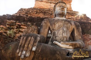 Seated Buddha at Wat Mahathat temple with sun